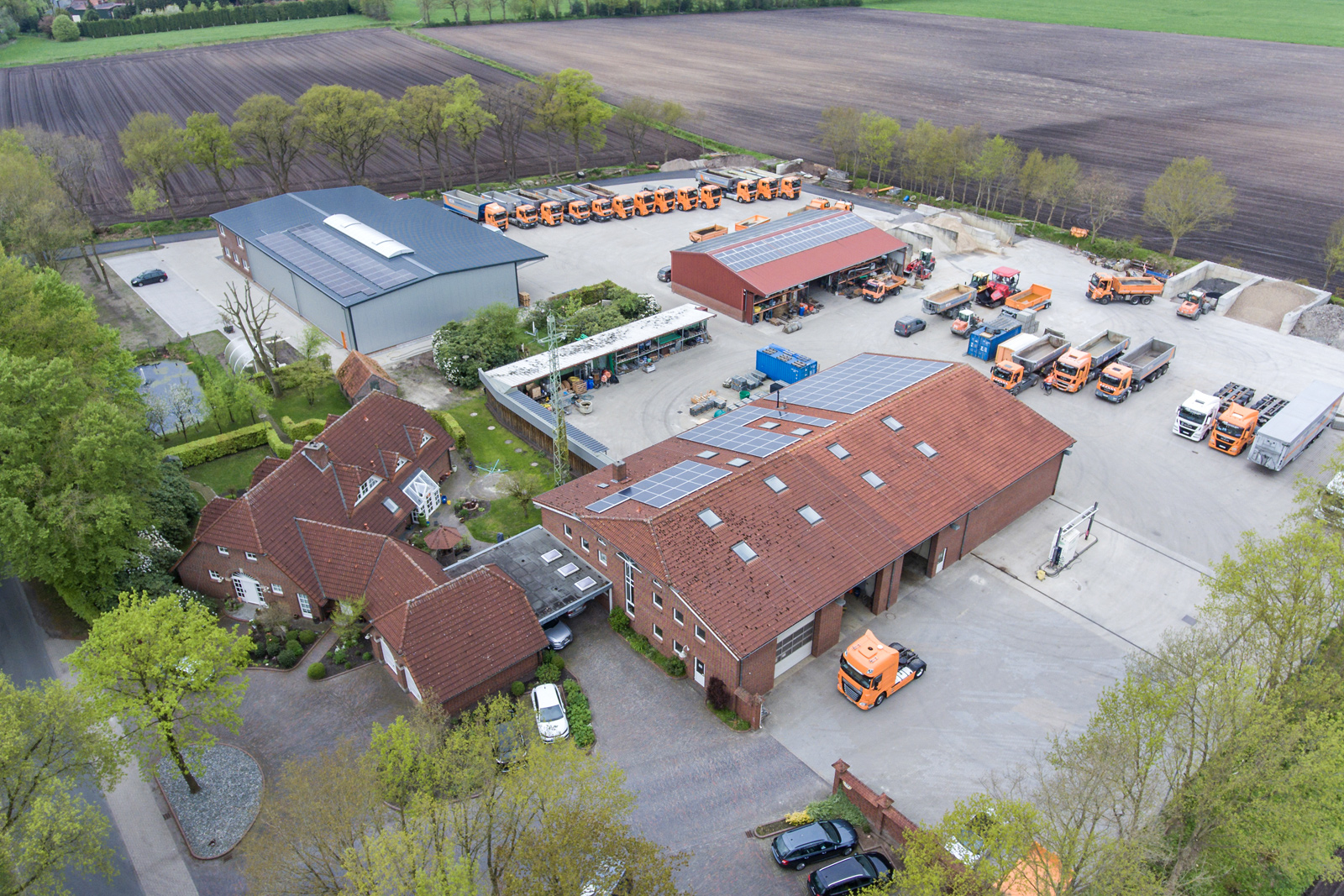 Über uns: Luftbild des Betriebsgeländes der Manfred Ende GmbH mit modernem Fuhrpark, mehreren Hallen, Bürogebäuden und großen Arbeitsflächen. Zahlreiche LKWs und Maschinen zeigen die Leistungsfähigkeit des Unternehmens in den Bereichen Transport, Tiefbau und Baustoffhandel. Manfred Ende - Baustoffhandel & Transporte
