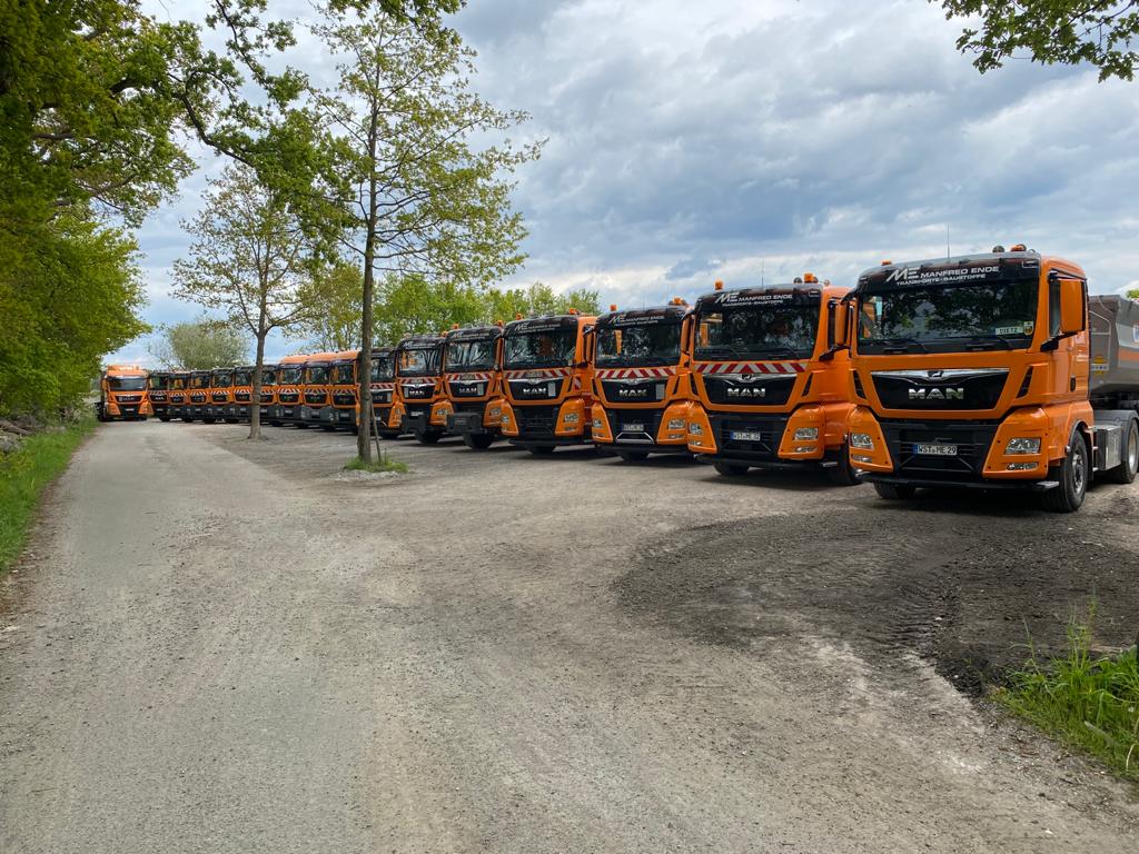 Fuhrpark von Manfred Ende – Baustoffhandel & Transporte mit mehreren orangefarbenen LKW im Einsatz.